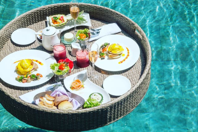 Desayuno servido en una bandeja flotante dentro de la alberca de una villa