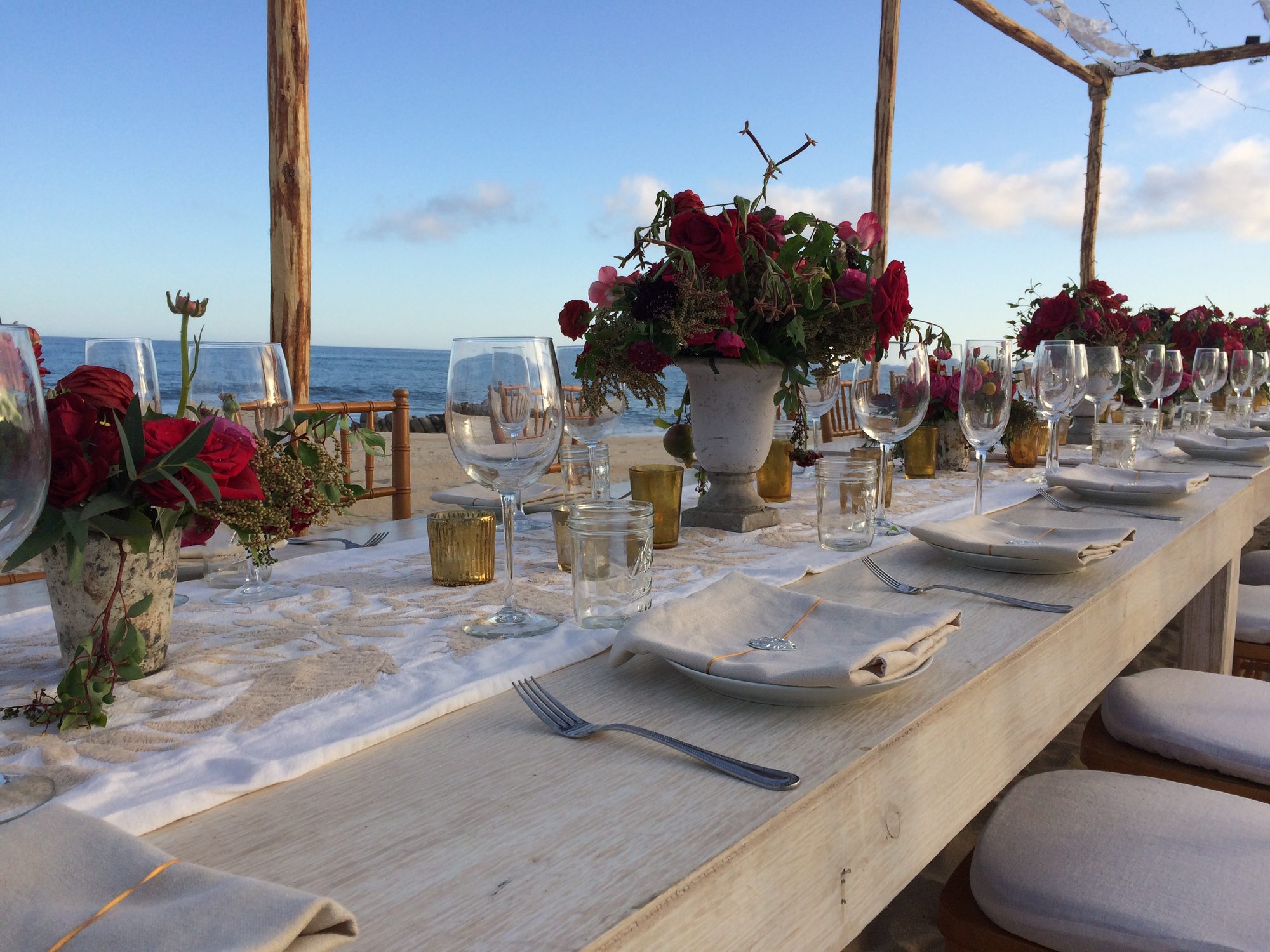 A long table set for dinner with flowers, wine glasses and linen napkins, overlooking the sea in Los Cabos