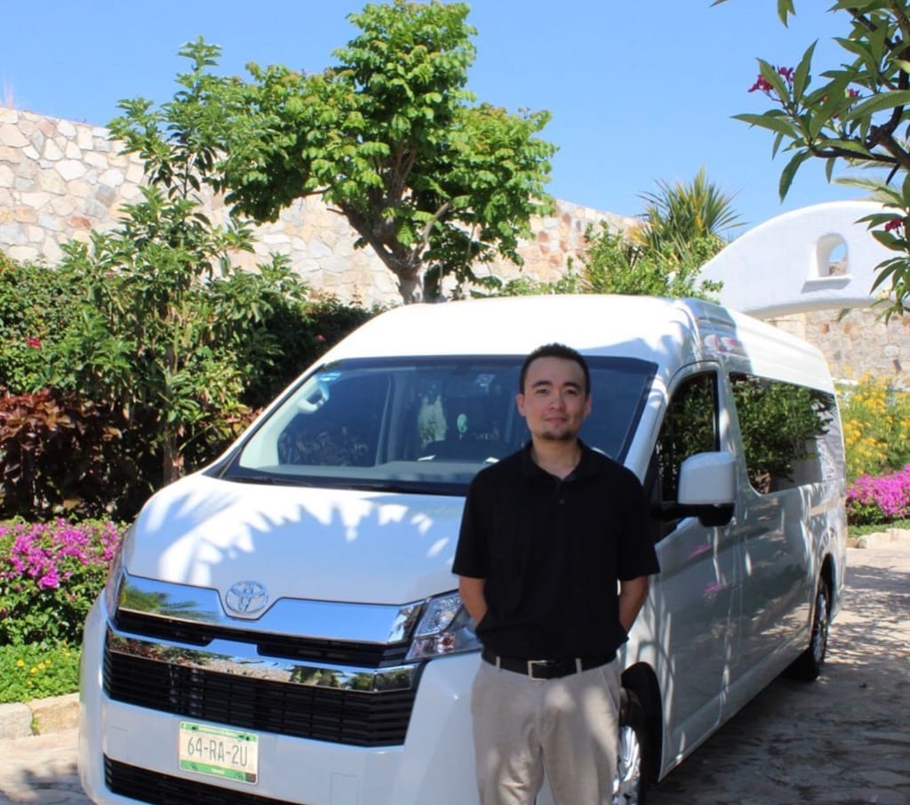 A Cabo Travel Boutique driver standing beside a white passenger van at a villa entrance in Los Cabos
