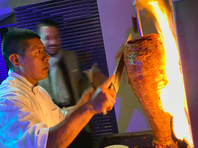 A live taquero carving al pastor off the trompo